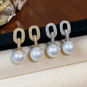 Close-up of zircon-encrusted oval hoop earrings with white pearls in gold and silver.