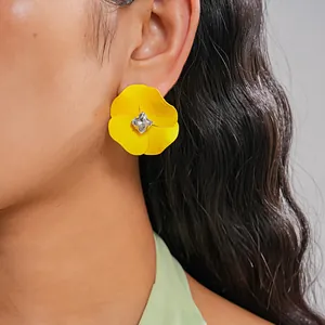 Close-up detail of a bright yellow painted flower stud earring with central crystal on model