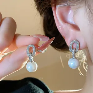 Close-up view of zircon oval pearl drop earrings worn on an ear with elegant lighting