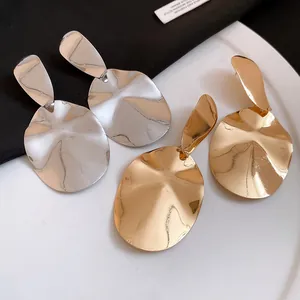 Detailed close-up showing wavy metallic oval drop earrings in gold and silver finishes
