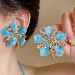 Macro detail of oversized blue drip oil flower earrings with gold metallic folds