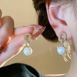 Close-up of elegant French-style gold oval stud earrings with dangling white pearls