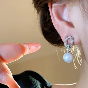 Detailed shot of elegant silver zircon earrings with dangling white pearl on ear.