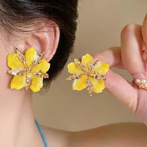 Detailed view of yellow pleated flower stud earrings with gold metallic stamen on ear
