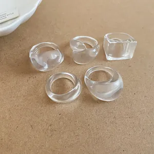 Detail view of five clear resin rings with irregular geometric shapes on beige background