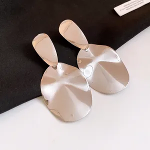 Close-up of shiny silver metallic oval earrings with modern wavy texture detail