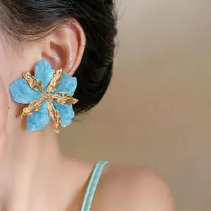 Detailed view of an oversized blue pleated flower stud earring on a female model's ear