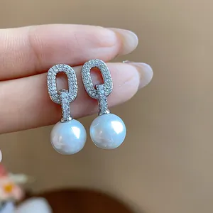 Close-up of elegant oval zircon earrings with glossy white pearls in detail view.