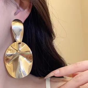 Close-up of large glossy golden oval drop earrings with unique wavy metal texture on ear.