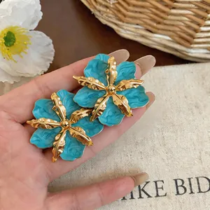 Detailed view of turquoise and gold flower stud earrings with a vintage enamel finish.