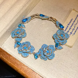 Elegante bracciale con rose blu e zirconi a goccia presentato in una scatola vintage.