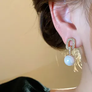 Close-up of elegant French style zircon oval gold stud earrings with white pearl drop detail