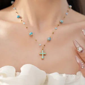 Close-up of a vintage-style turquoise beaded cross necklace with a golden chain finish.