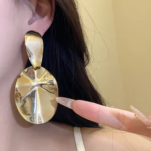 Close-up detail of oversized shiny gold oval drop earrings worn on model for party