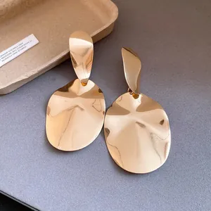 Close-up of gold irregular oval drop earrings with polished finish and metallic texture