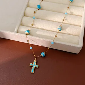 Close-up of a blue enamel cross pendant on a beaded gold chain with stone beads
