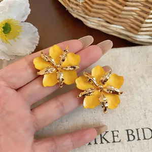 Detailed view of bold yellow enamel flower stud earrings with textured gold metallic petals