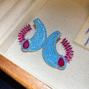 Dettaglio macro di orecchini a mezzaluna con perline turchesi e pietre magenta.