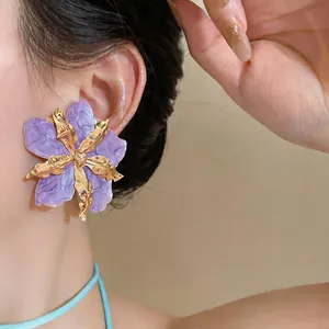 Close-up detail of oversized purple oil-dripped flower earrings with gold finish.