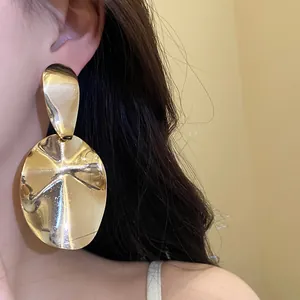 Professional close-up of glossy gold irregular oval metal drop earrings worn by a model.