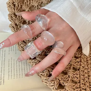 Close-up of chunky transparent resin rings set on a hand over a woven mat background