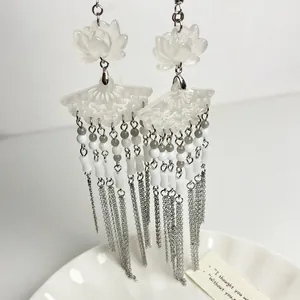 Detailed close-up of white lotus fan earrings with long silver tassels and gray beads