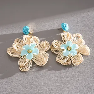 Close-up view of handmade woven raffia flower earrings with light blue fabric centers