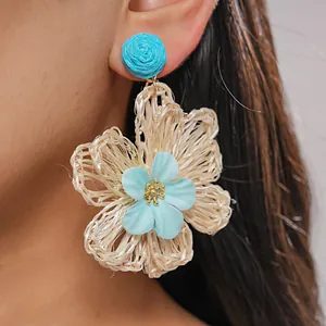 Detailed close-up showing the intricate texture of blue and beige woven raffia flower earrings.