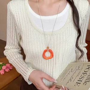 Dettaglio della collana con ciondolo geometrico in acrilico arancione su maglione