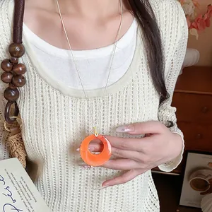Dettaglio di una collana con ciondolo circolare in acrilico arancione acceso.