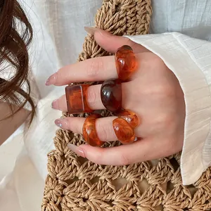 Detail view of chunky amber resin rings in varied geometric shapes on a model's hand.