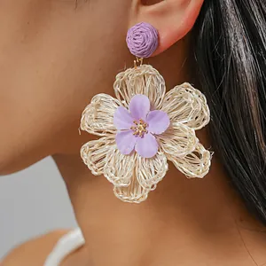 Close-up of hand-woven raffia flower earrings in purple and white, vacation style
