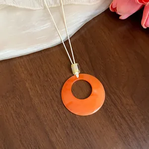 Dettaglio di una collana con ciondolo circolare in acrilico arancione vivace e cordino bianco