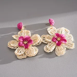 Detailed macro shot of handmade woven raffia flower earrings in cream and magenta tones