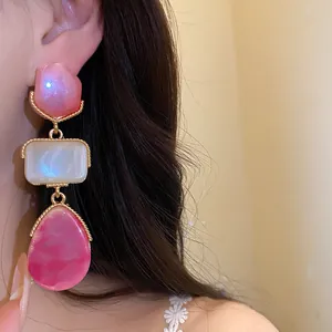 Détail macro de boucles d'oreilles pendantes vintage en résine rose nacré et blanc.