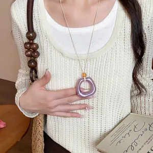 Dettaglio della collana con ciondolo geometrico in acrilico viola su un maglione