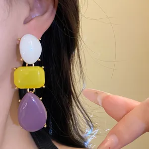 Close-up of three-tier resin drop earrings with white, yellow, and purple geometric shapes