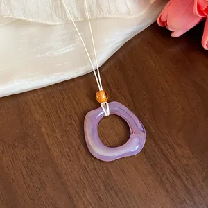 Primo piano di una collana con ciondolo geometrico in acrilico viola e cordoncino in pelle.