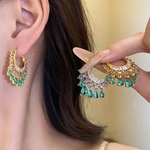 Close-up detail of ornate gold hoop earrings featuring green waterdrop pendants and purple zircons