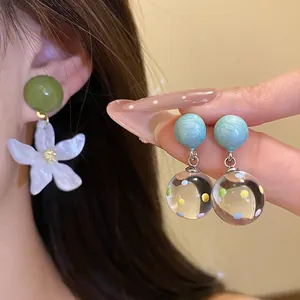 Close-up detail of forest-style resin flower earrings and colorful polka dot ball drop earrings