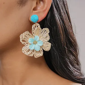 Close-up of handmade woven raffia flower earrings with blue fabric petal detail