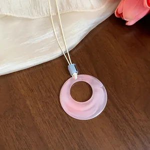 Primo piano di una collana con pendente in acrilico rosa e cordino in pelle crema minimal.