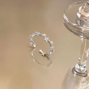 Detailed macro view of a silver-finish open ring with zircon flower motifs on a reflective surface.