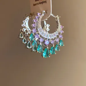 Detail view of silver hoop earrings with purple and teal zircon teardrops