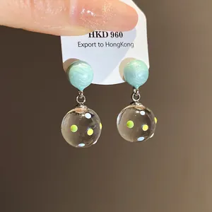 Close-up view of mint resin drop earrings with multi-colored polka dot glass balls.