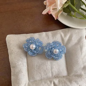 Detalle de pendientes de flor con cuentas azul claro y perla blanca en el centro