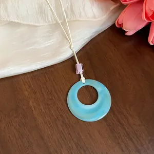 Dettaglio di collana con pendente in acrilico blu circolare e cordoncino crema su legno.