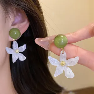 Detailed macro view of white resin flower earrings with green sphere base worn on ear