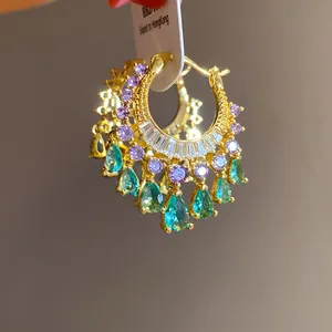 Detail view of gold-plated hoop earrings with purple stones and green crystal drops