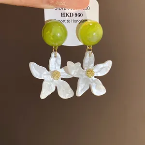 Close-up of green resin ball and white flower drop earrings with marble texture